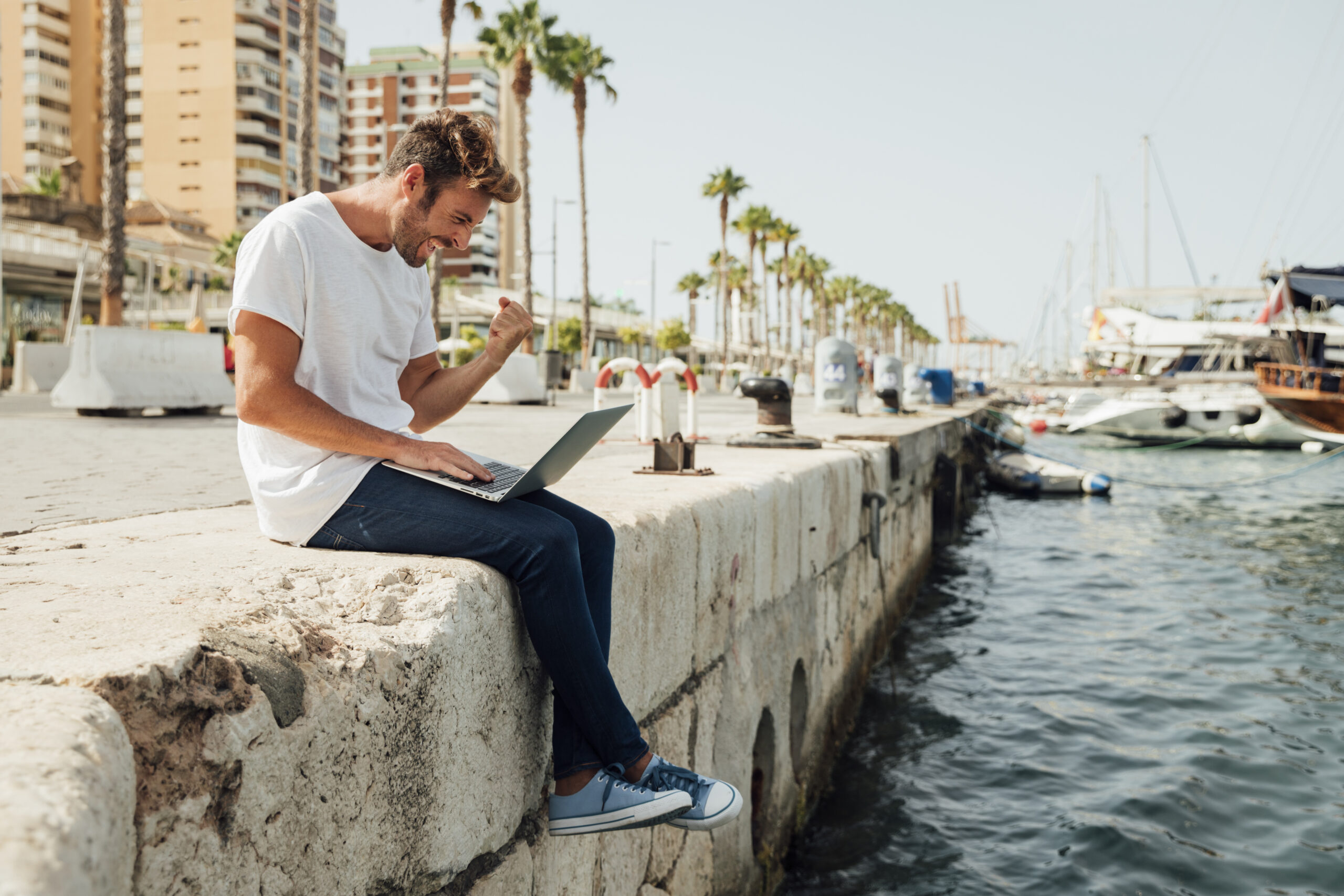 man with laptop celebrating by river scaled